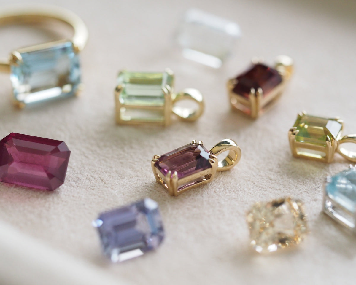 Two octagonal shape gemstone pendants, one in yellow gold and one in silver, displayed on a textured beige surface.