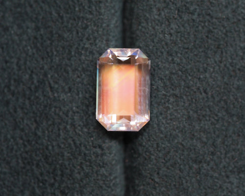 A rainbow moonstone emerald cut sits in front of a green velvet background