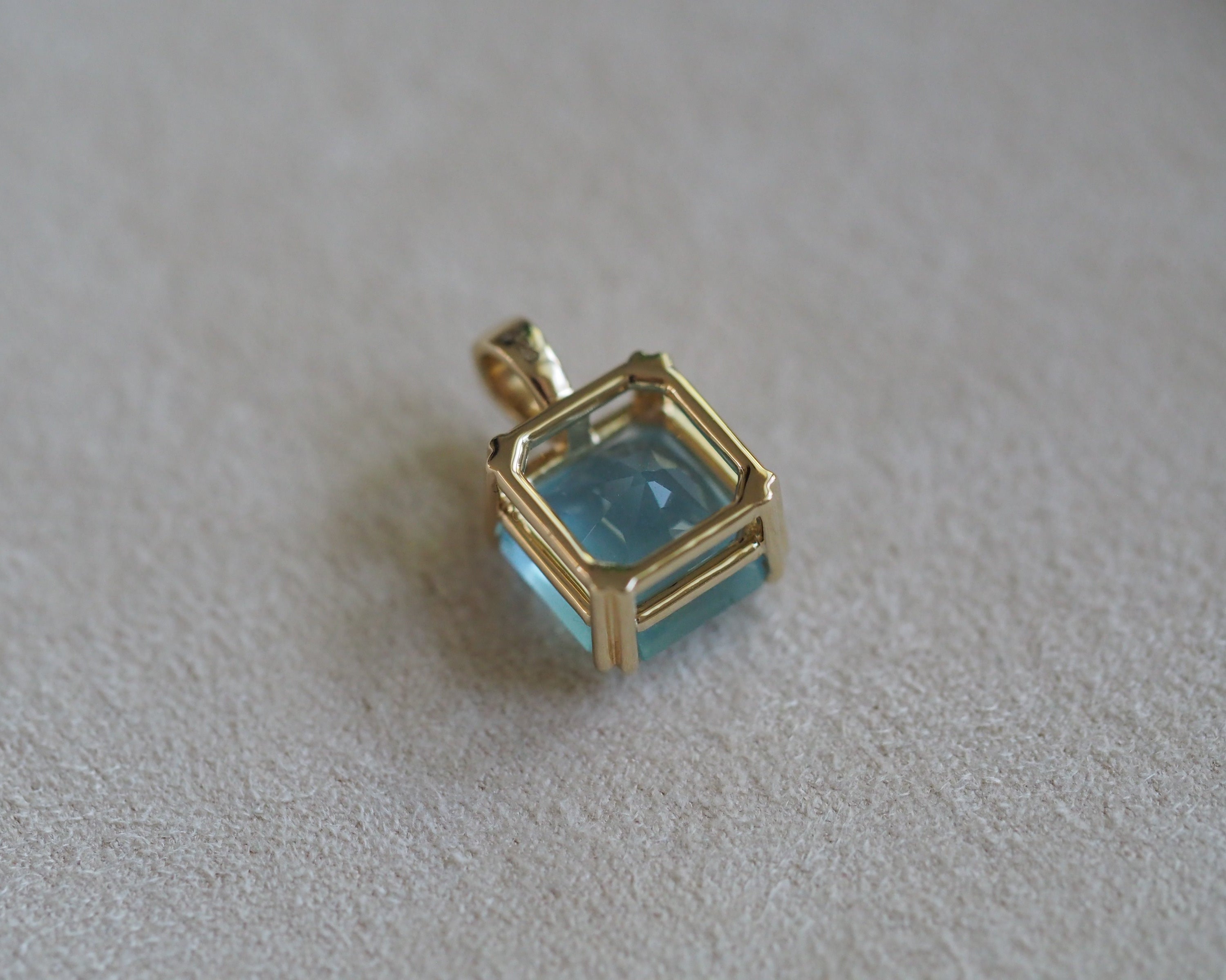 Back of Carolyn Asscher Aquamarine pendant in front of a beige background