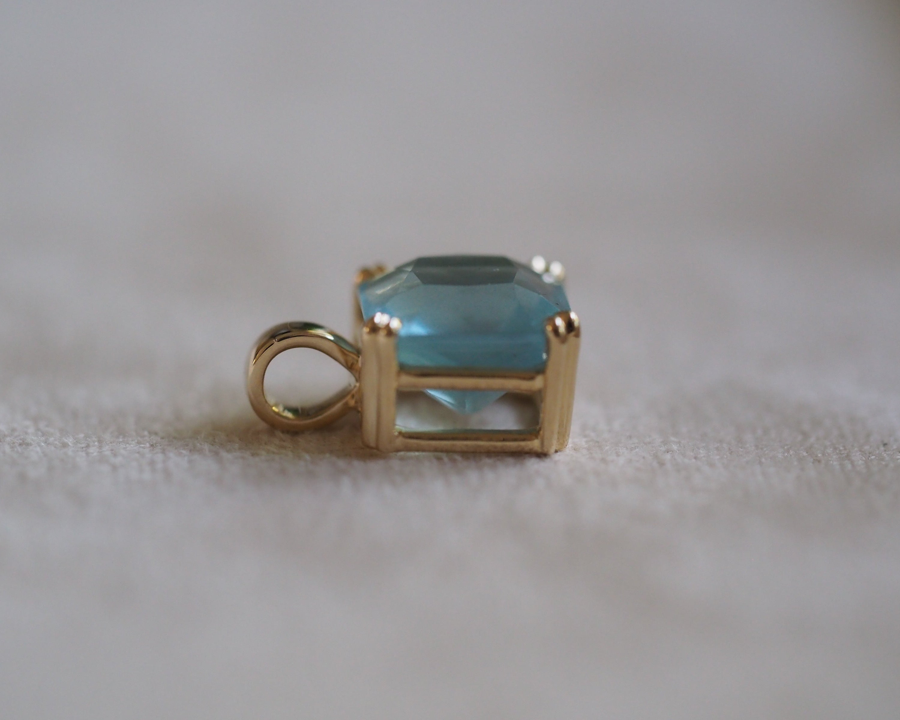 Side Carolyn Asscher Aquamarine pendant in front of a beige background