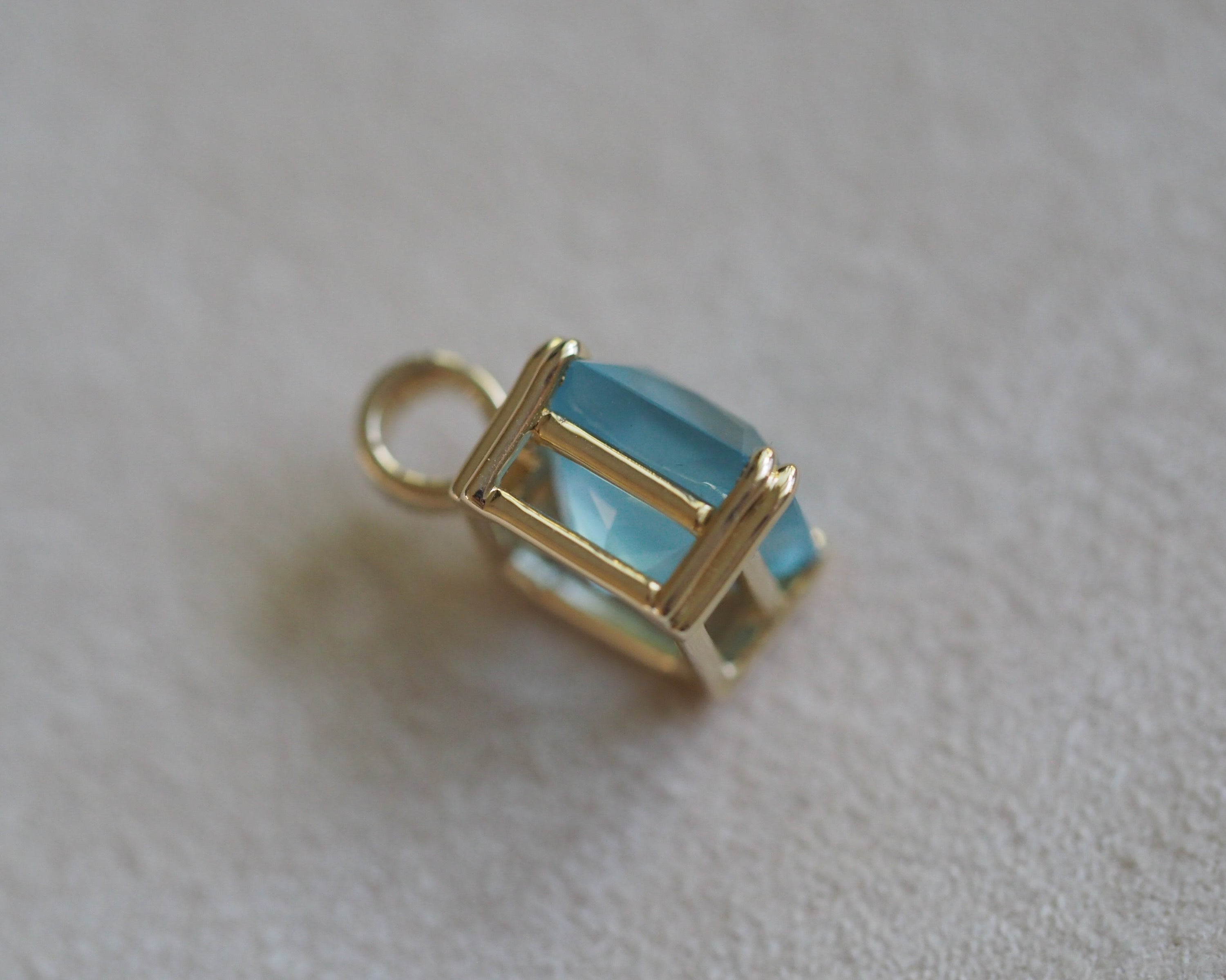 Side of Carolyn Asscher Aquamarine pendant in front of a beige background