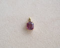 A rectangular pink spinel pendant set in a gold bezel, displayed on a textured light beige surface.