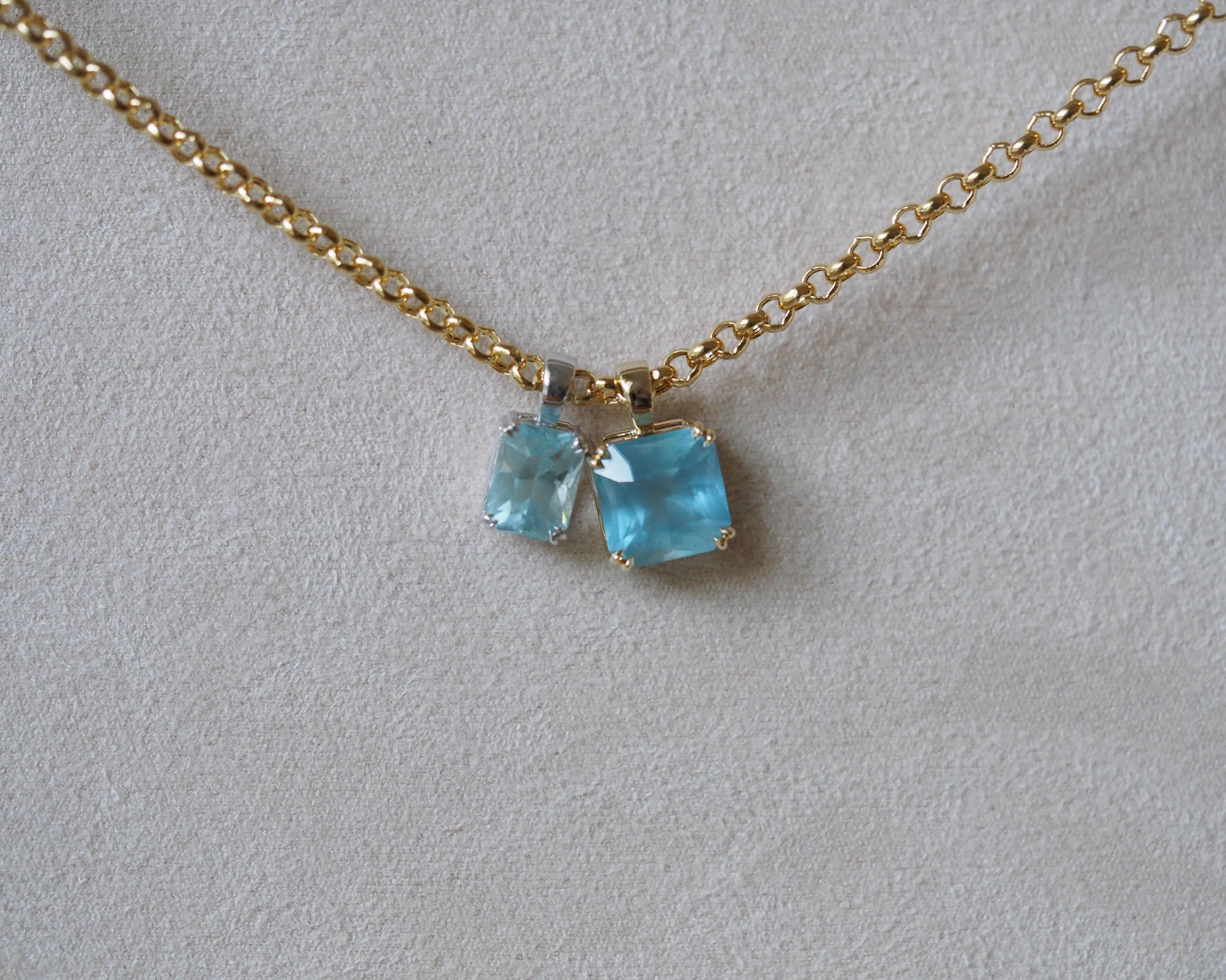 Carolyn Radiant aquamarine pendant in front of a beige background with chain styled with Carolyn Asscher aquamarine pendant