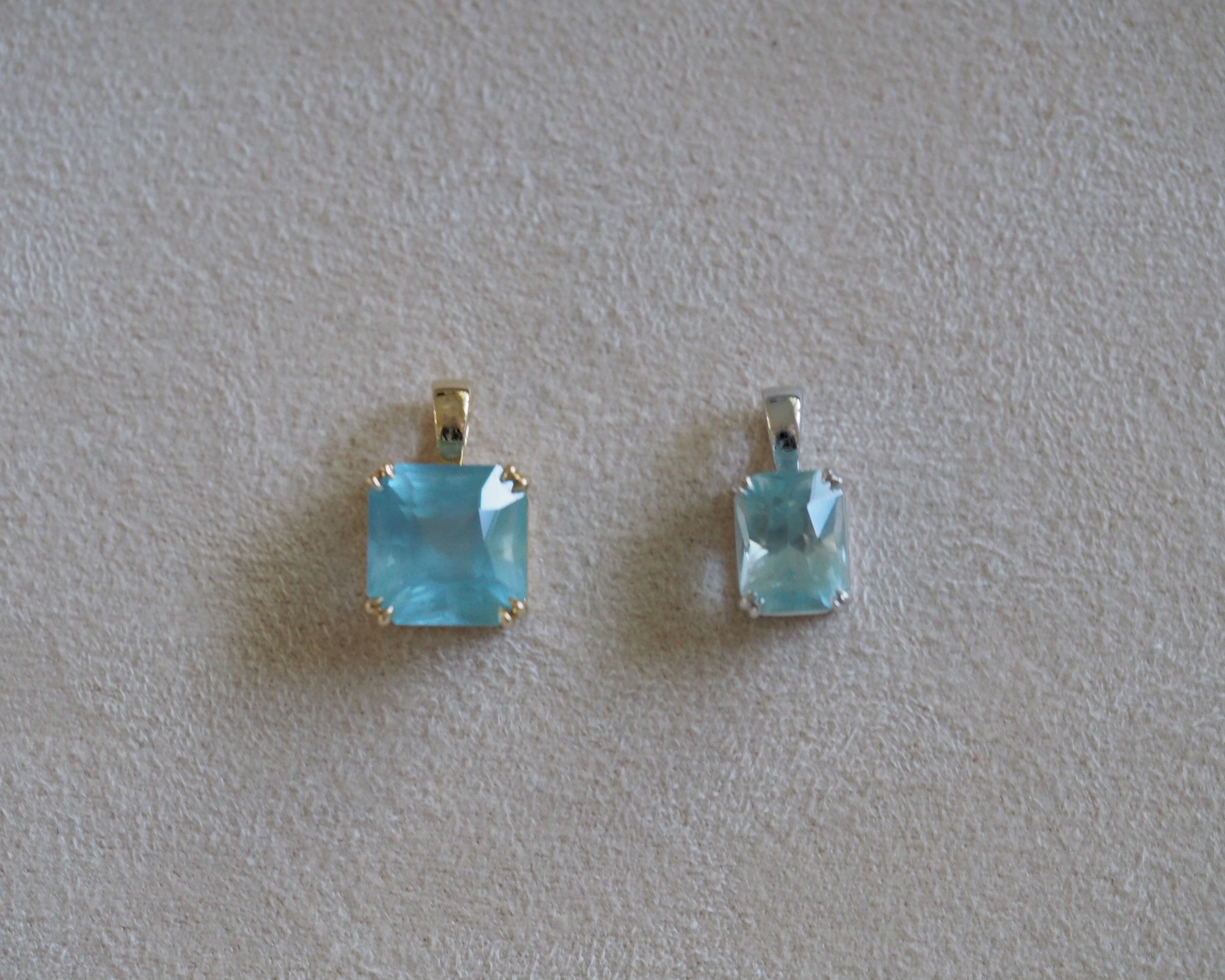 Carolyn Asscher Aquamarine and Carolyn radiant aquamarine pendant in front of a beige background