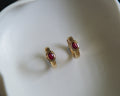 Pair of gold earrings with red stones on a white surface