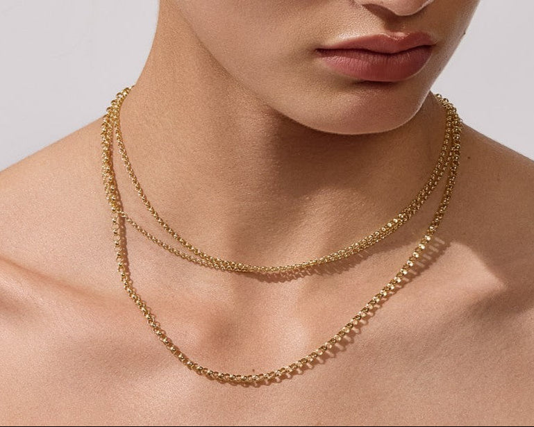 Woman wearing a gold necklace and earrings against a neutral background