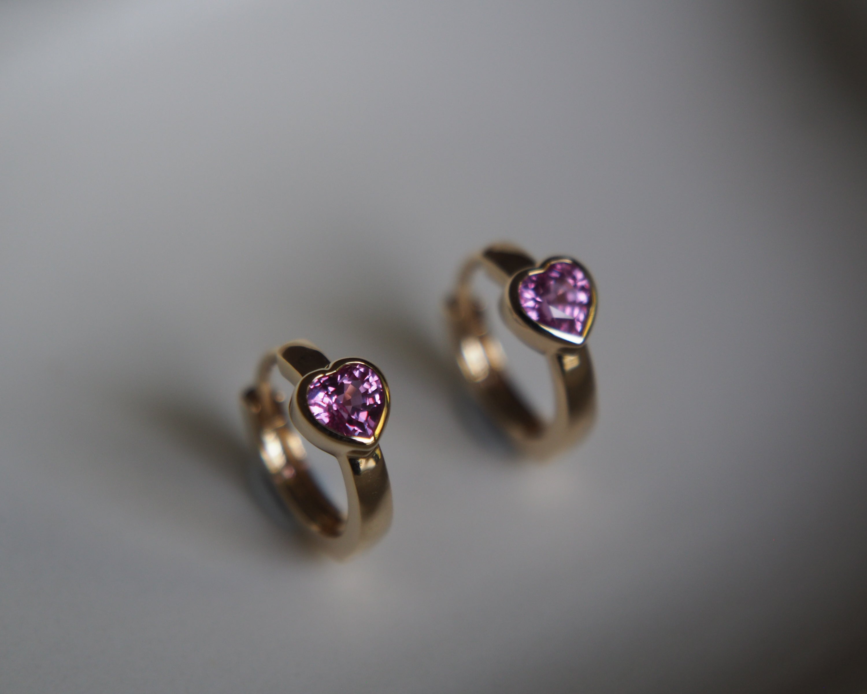Gold hoop earrings with heart-shaped purple gemstones on a gray background