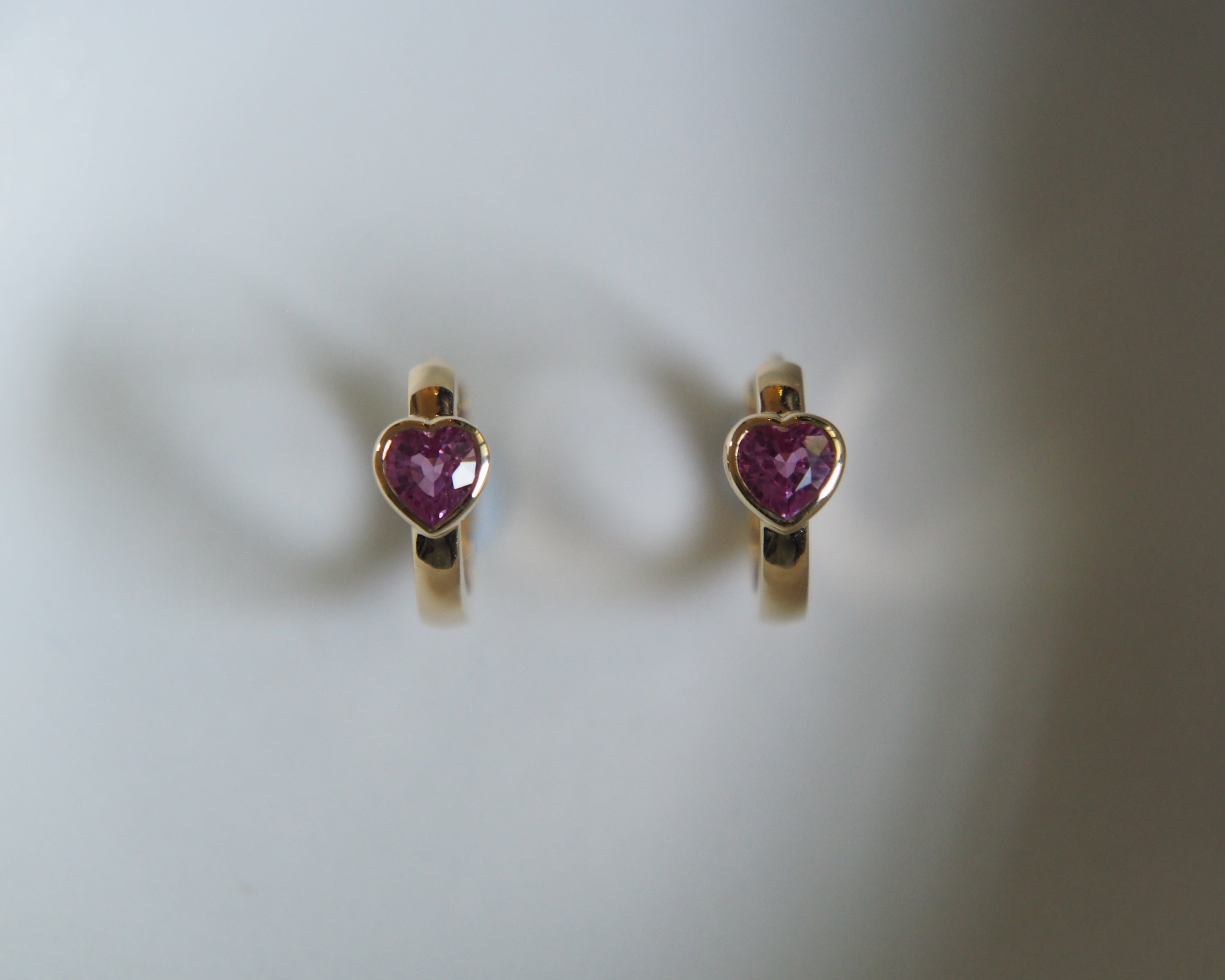 Heart-shaped earrings with purple gemstones on a light gray background