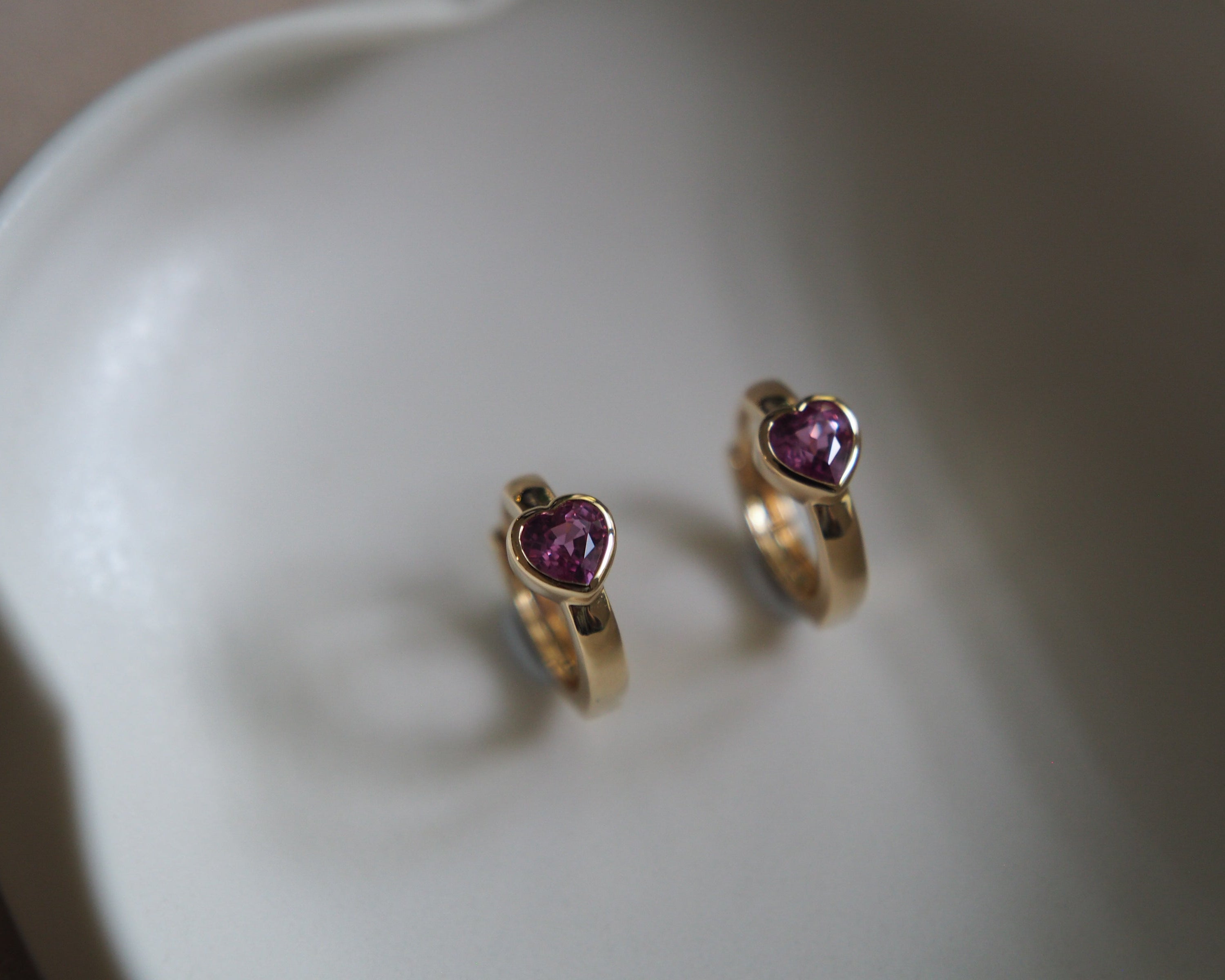 Gold hoop earrings with purple gemstones on a white dish