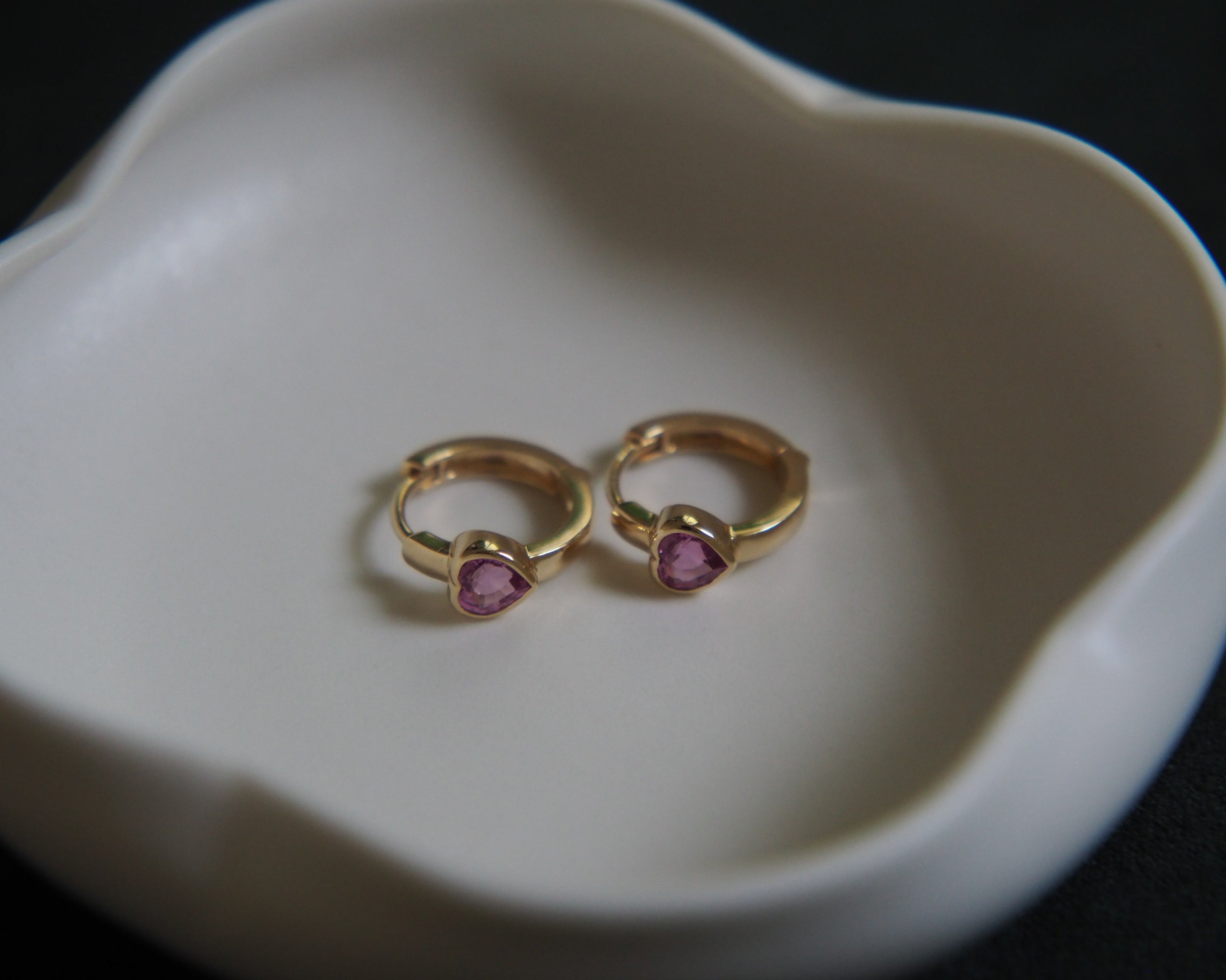 Gold earrings with pink gemstones on a white dish.