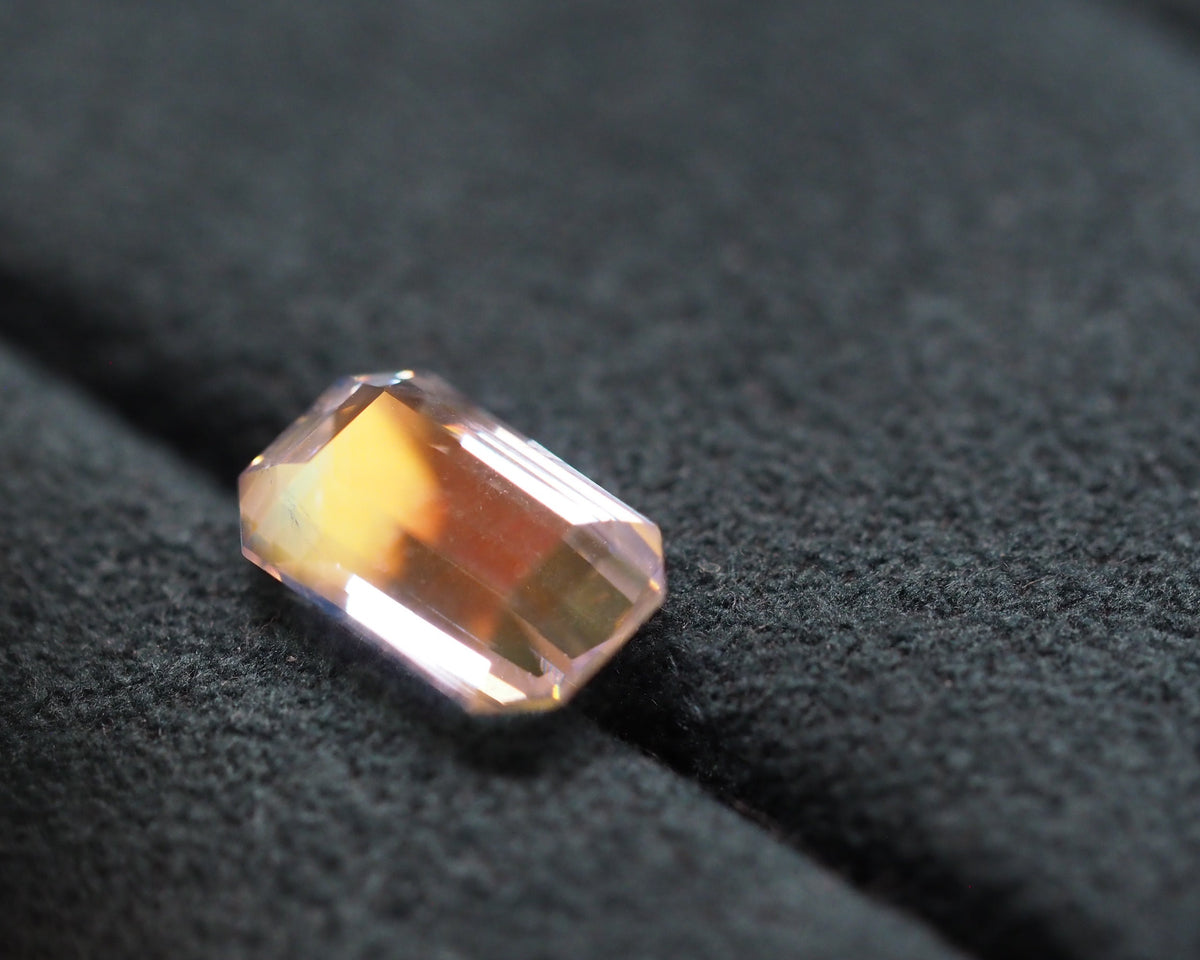 A rectangular emerald-cut peach-colored gemstone resting on a textured black velvet surface.