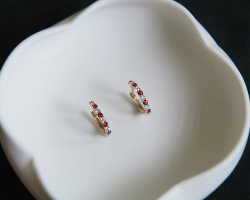 Pair of gold earrings with red gemstones on a white dish.