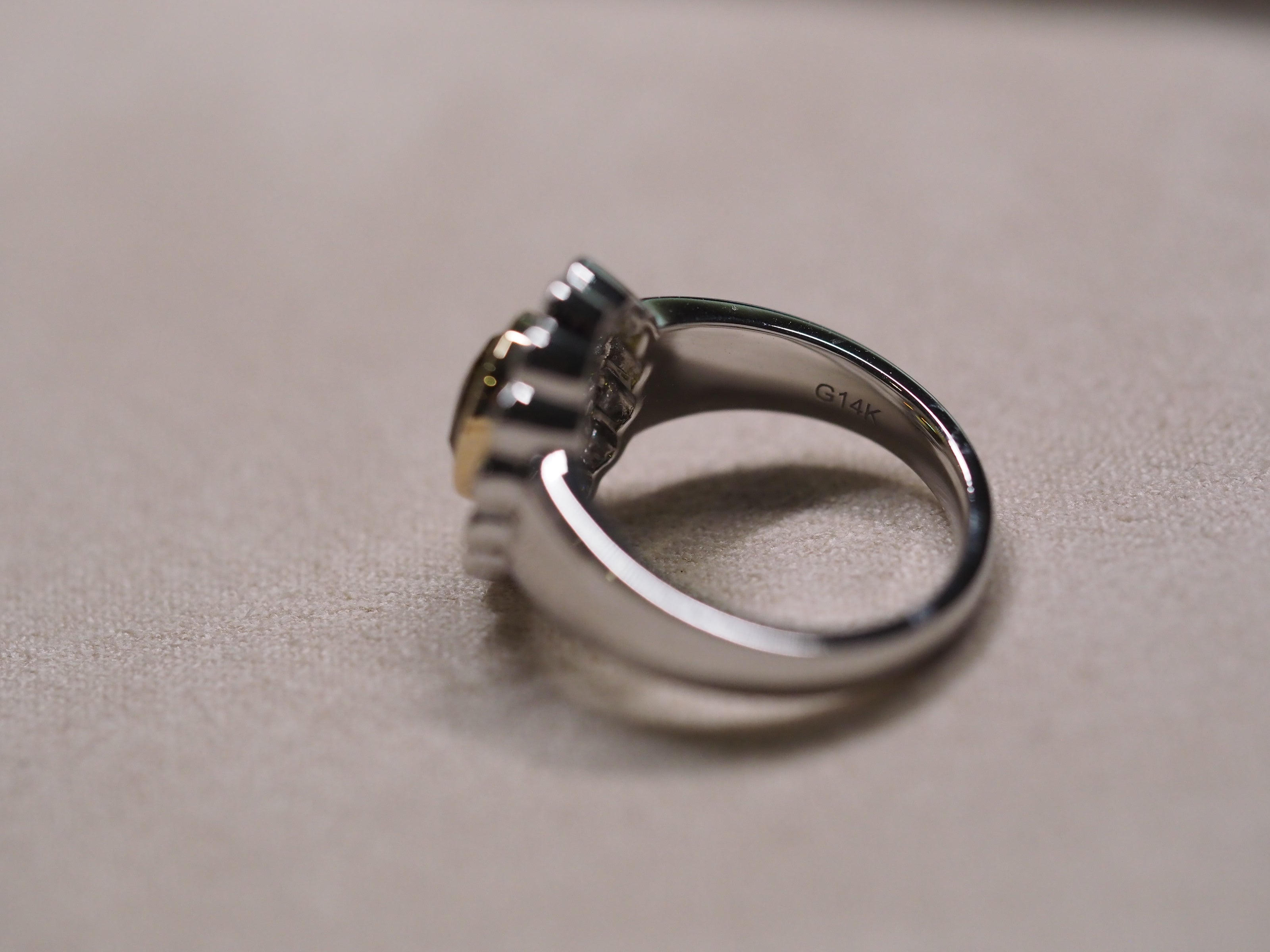 A silver-toned ring with a multi-prong setting and a small gold accent on the band, resting on a textured beige surface.